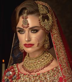 a woman wearing a red and gold bridal outfit with jewelry on her head, in front of a dark background