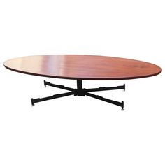 an oval wooden table with black legs and wheels on the bottom, against a white background