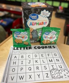 two bags of alphabet cookies sitting on top of a table next to a box of letters