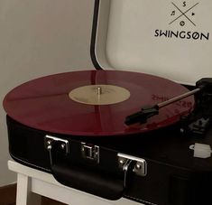 a red and black record player sitting on top of a white table next to a suitcase