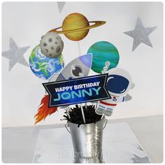 a happy birthday sign is placed in a vase filled with balloons and other items that are on top of the cake