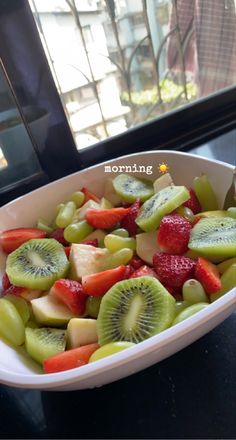 a white bowl filled with sliced fruit on top of a table next to a window