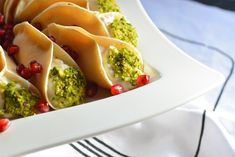 a white plate topped with dumplings covered in broccoli and pomegranate