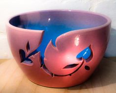 a pink and blue bowl sitting on top of a wooden table next to a white wall