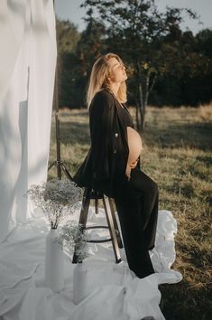 a pregnant woman sitting on a chair in front of a white drape and flowers