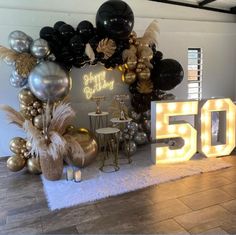 a 50th birthday party with balloons and lights on the wall, gold and black decorations