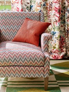 a chair with a pillow on top of it in front of some curtains and rugs