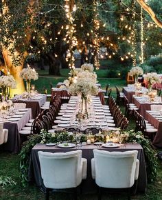 an outdoor dinner table set up with white flowers and greenery on the tables, surrounded by string lights