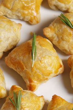 small pastries with rosemary sprigs on top are arranged on a white plate