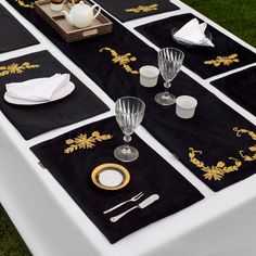 black and gold placemats are set on a white tablecloth with silverware