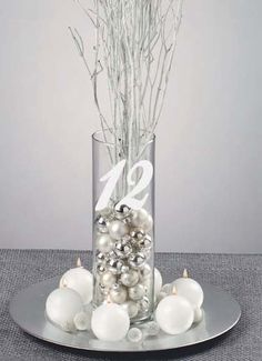 a glass vase filled with ornaments on top of a silver plate and surrounded by white balls