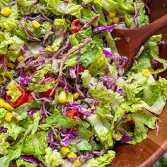 a salad with lettuce, corn and tomatoes in a wooden bowl