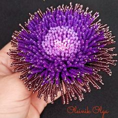 a hand holding a purple flower with lots of tiny beads on it's center