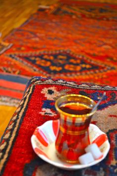 a red and white cup sitting on top of a saucer next to a rug