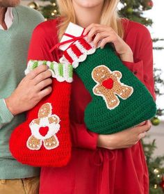 a man and woman holding christmas stockings with gingerbreads on them, in front of a christmas tree