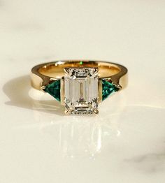 This emerald three-stone engagement ring is all custom from head to toe. Let's break it down: ⁠⁠• Lab grown green emerald trillion side stones⁠ • 2.1ct, D Color, VVS2 Center Emerald⁠ Diamond • 3.5mm Square band that tapers into cathedral shoulders⁠ • Our signature Breezy setting, to top it off ✨⁠ �• All set in a shiny 18k Yellow Gold⁠ Royal Emerald Cut Diamond, Green Diamond Wedding Ring, Ethereal Rings, Emerald Green Engagement Ring, Diamond Ring With Emerald, Three Stone Engagement Rings Emerald, Frank Darling, Emerald Engagement Ring Green, Emerald Wedding Band