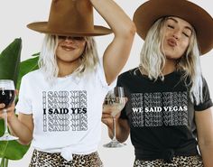 two women wearing matching tshirts and hats holding wine glasses in front of their faces