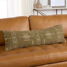 a brown leather couch with a decorative pillow on it's back and a white vase in the background