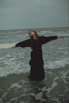 a woman standing in the ocean with her arms outstretched