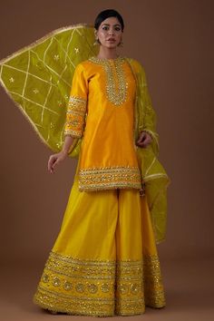 Amber glow serenade A-line kurta with gota, sequins and pearls hand embroidery. Comes with sharara and a mist green dupatta.
Components: 3
Pattern: Hand embroidered
Type Of Work: Gota, Sequins, Pearls
Neckline: Round
Sleeve Type: Three quarter
Fabric: Dupion silk, Dupatta : Organza
Color: Yellow
Other Details: 
Model Height : 5 ft 7 inches, wearing size M
Closure : Kurta - Front buttons
Occasion: Sangeet - Aza Fashions Dholki Dress, Jaggo Outfit, Green Suit Women, Diwali Dress, Indian Fits, Haldi Dress, Green Dupatta, Long Blouse Designs, Diwali Dresses