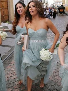 three women in blue dresses are walking down the street with white flowers on their bouquets