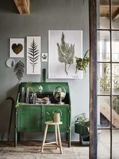 a green cabinet in a room with plants on the wall and pictures hanging above it