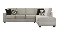 a white sectional couch with black and gray pillows on the armrests next to a footstool