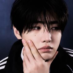 a young man with black hair and white shirt holding his hand to his face while looking at the camera