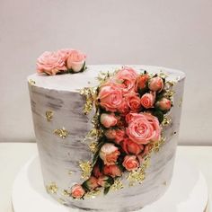 a white cake with pink flowers on top and gold decoration around the edges, sitting on a table