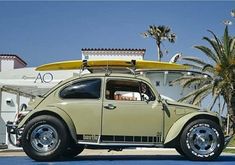 an old vw bug is parked in front of a building with surfboards on top