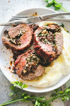 a white plate topped with meat and mashed potatoes next to a knife and fork