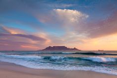 an ocean beach with waves coming in to shore and a mountain in the distance at sunset