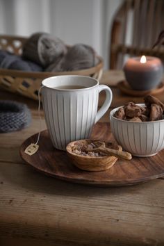 two white cups filled with food sitting on top of a wooden tray next to yarn