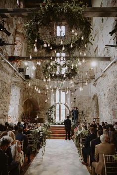 a wedding ceremony in an old building with chandeliers and greenery hanging from the ceiling