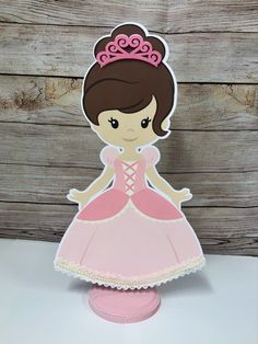 a paper cut out of a princess standing on top of a wooden table with a pink dress