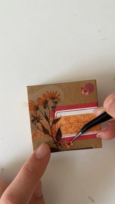 a hand holding a black pen over a piece of brown paper with flowers on it