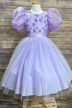 Petite Adele This tea-length girls' dress features organza bubble sleeves, a dazzling floral sequin bodice, and a luxurious tulle & satin skirt. Add an optional satin bow for an unforgettable look! The dress is fully lined and includes additional netting under the skirt to give it an extra fluffy look! Includes a satin waistband to ensure a perfect fit. Purple Princess Dress With Floral Applique For Parties, Tulle Pageant Dress With Floral Applique For Dress-up, Spring Princess Style Fitted Ball Gown, Fitted Princess Ball Gown For Spring, Princess Style Fitted Ball Gown For Spring, Spring Princess Dress With Fitted Bodice And Tulle, Spring Prom Princess Dress, Spring Ball Gown For Dress-up, Fitted Princess Dress With Floral Applique