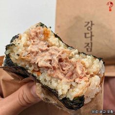 a person holding up a piece of food with meat and rice in it's wrapper