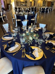 the tables are set up with blue linens and gold place settings for an elegant dinner