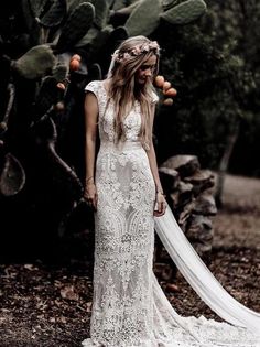 a woman standing in front of a cactus wearing a wedding dress with an open back