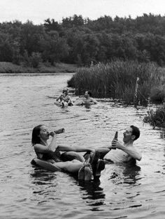 black and white photograph of people floating in water with one person holding a beer bottle