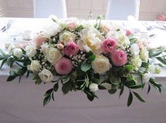 a bouquet of white and pink flowers sitting on top of a table with chairs in the background