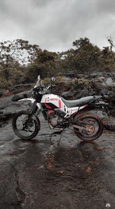 a dirt bike parked on top of a rocky hill next to some trees and bushes