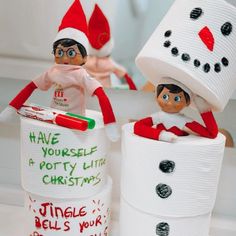 two elfs are sitting on top of toilet paper rolls and one is holding a toothbrush