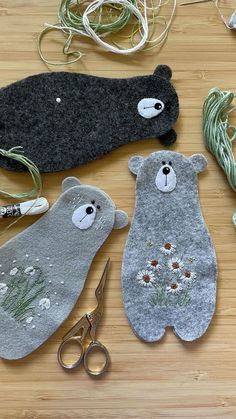 three bears made out of felt sitting on top of a wooden table next to scissors and yarn