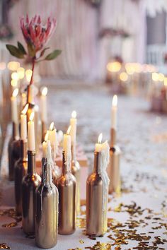 there are many bottles with flowers in them and candles on the table next to each other