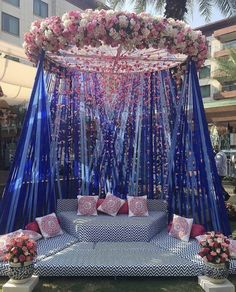 an outdoor wedding setup with blue and pink flowers on the canopy, surrounded by pillows