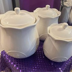 three white dishes with lids sitting on purple sequins