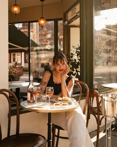 a woman sitting at a table in front of a window with wine glasses on it