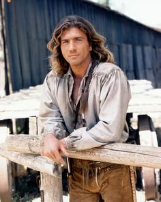 a man with long hair leaning on a fence